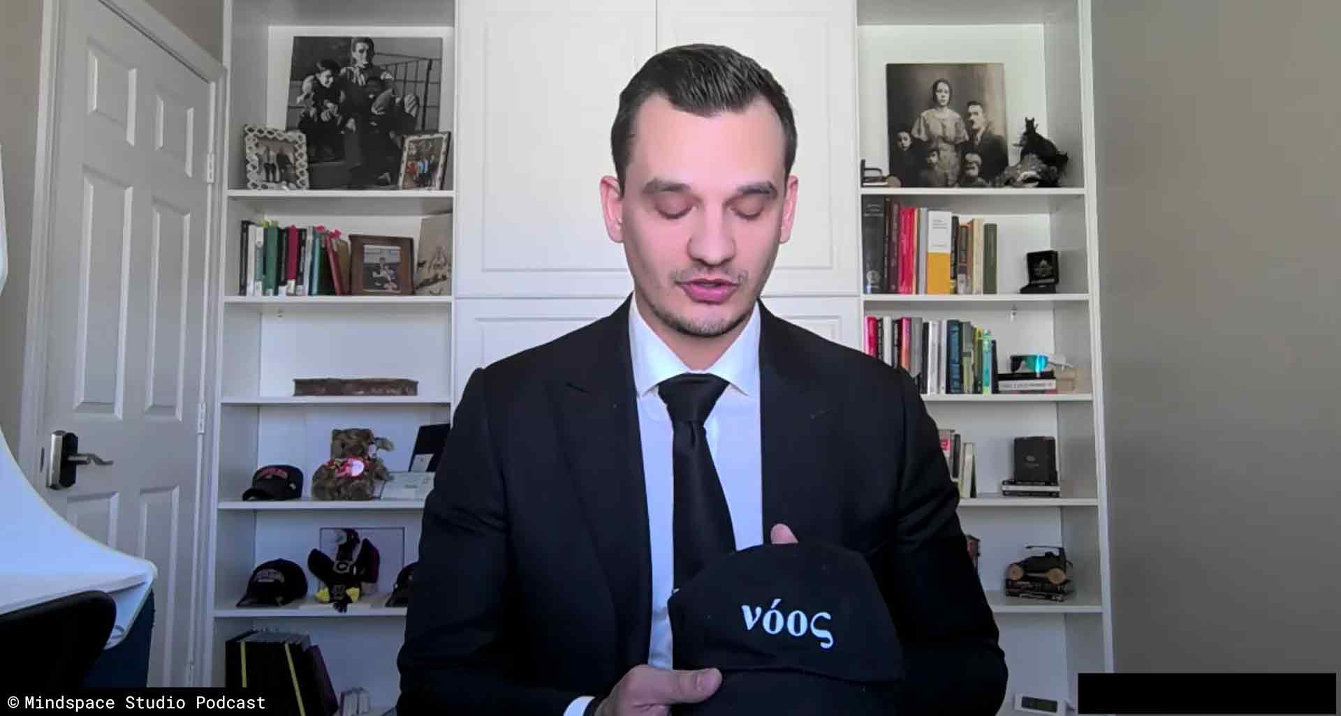 Boban Dedovic explaining noos in Homeric Greek while wearing a black suit on his podcast
